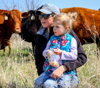 Female rancher and her daughter crouch in pasture with cows